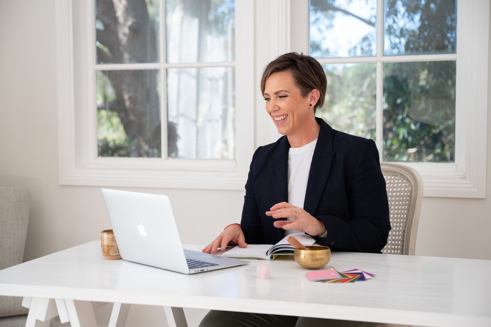 Anita Gibbons smiling during an online session, with a singing bowl and crystals on her desk