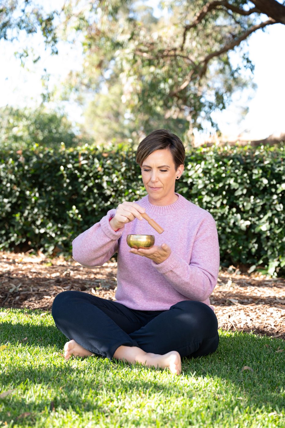 Anita Gibbons sitting cross-legged outdoors, playing a singing bowl